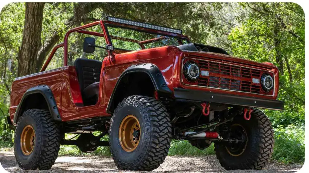 a red ford bronco is parked on a dirt road