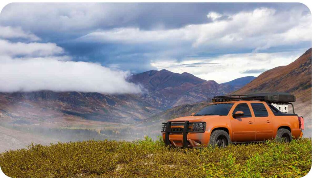 an orange pick-up truck is parked on the side of a mountain.